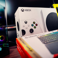 Xbox gaming console packaging with a blurred gaming setup in the background